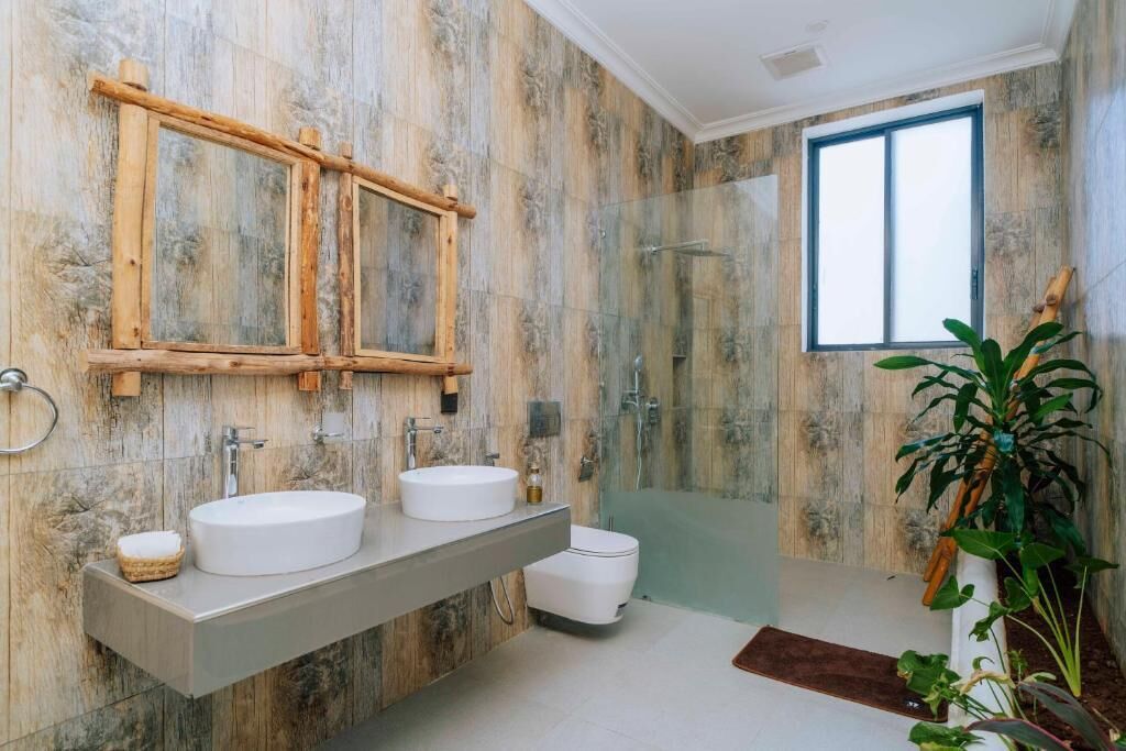A bathroom with a wooden vanity, two sinks, a toilet, a glass shower enclosure, and a window.