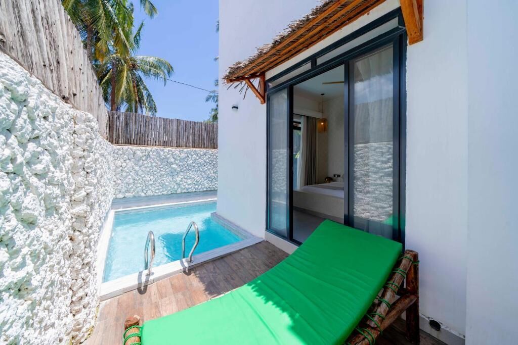 A private pool with a wooden deck, a lounge chair, and a glass door leading to a bedroom.