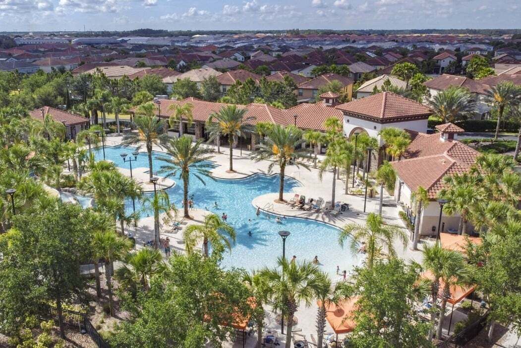 A resort with a central swimming pool, palm trees, and a view of surrounding houses.