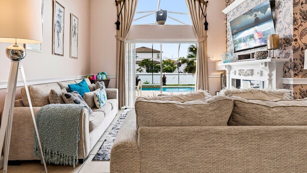 Ein Wohnzimmer mit Sofa, Fernseher, Lampe und Blick auf einen Pool.