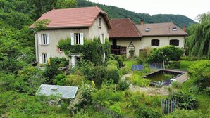 A two-story house with a red roof, surrounded by lush greenery and a small pond. - Stone house with treehouse and park in Valdaine (Saint-Geoire-en-Valdaine)