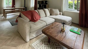 A spacious living room with a sofa, coffee table, and a dining area with a bench. - Stone house with treehouse and park in Valdaine (Saint-Geoire-en-Valdaine)