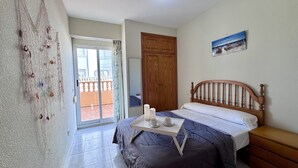 Un dormitori amb llit, capçalera de fusta, taula petita amb tasses, quadre a la paret i balcó amb vistes.