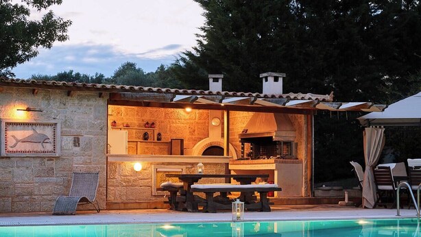 Edifici de pedra amb piscina, mobiliari d'exterior i forn de pizza.