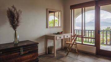 A room with a wooden dresser, a desk with drawers, a chair, a mirror, and a large window with a view.