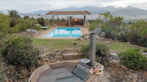 A hot tub with a stone wall, a pool, and a covered seating area with a fire feature. - Barton Hammerkop Villa nr Hermanus - Hottub & Pool (Bot River)