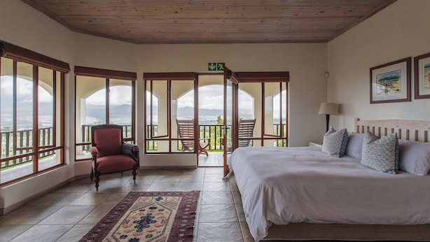 A bedroom with a bed, a chair, a rug, and large windows with a view. - Barton Hammerkop Villa nr Hermanus - Hottub & Pool (Bot River)