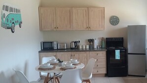 A kitchen with wooden cabinets, a microwave, a stove, and a dining table with chairs. - Barton Hoopoe Cottage Near Hermanus With Wood Fired Hot Tub (Bot River)