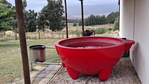 A red outdoor hot tub next to a building, with a metal container and a hose connected to it. - Barton Hoopoe Cottage Near Hermanus With Wood Fired Hot Tub (Bot River)