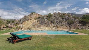 Una piscina con césped verde y una colina rocosa al fondo.