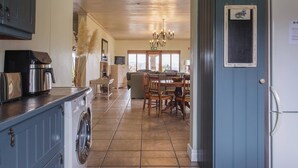 Una cocina con lavadora, cafetera y comedor con sillas y una mesa.