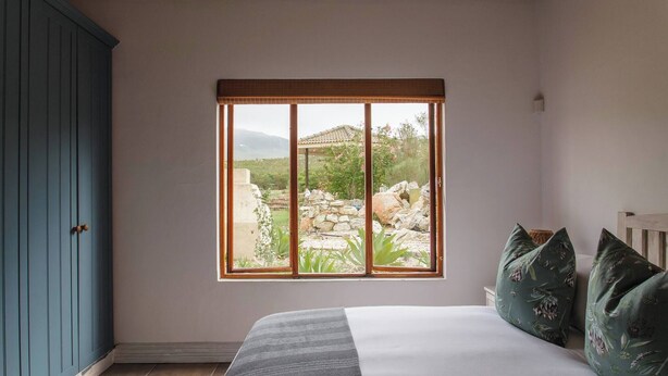 Un dormitorio con cama, ventana con vista a un jardín y un armario azul.