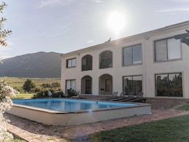 Un edificio de dos pisos con piscina, ventanas amplias y vista a las montañas.