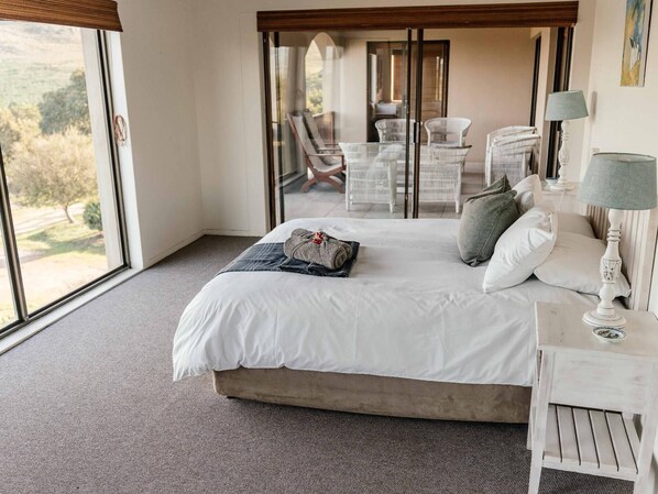 A bedroom with a large bed, a nightstand, a lamp, and a view of outdoor furniture through a glass door.