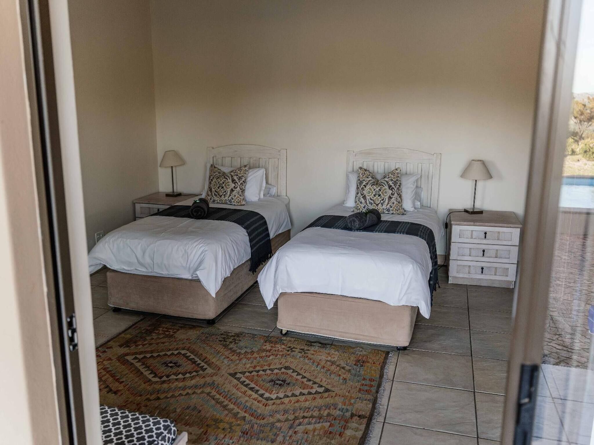 Une chambre avec deux lits, une table de chevet avec une lampe, une petite commode et un tapis à motifs.