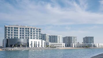 Un hôtel situé au bord de l’eau, composé de plusieurs immeubles de grande hauteur, avec une plage en arrière-plan et un ciel dégagé.