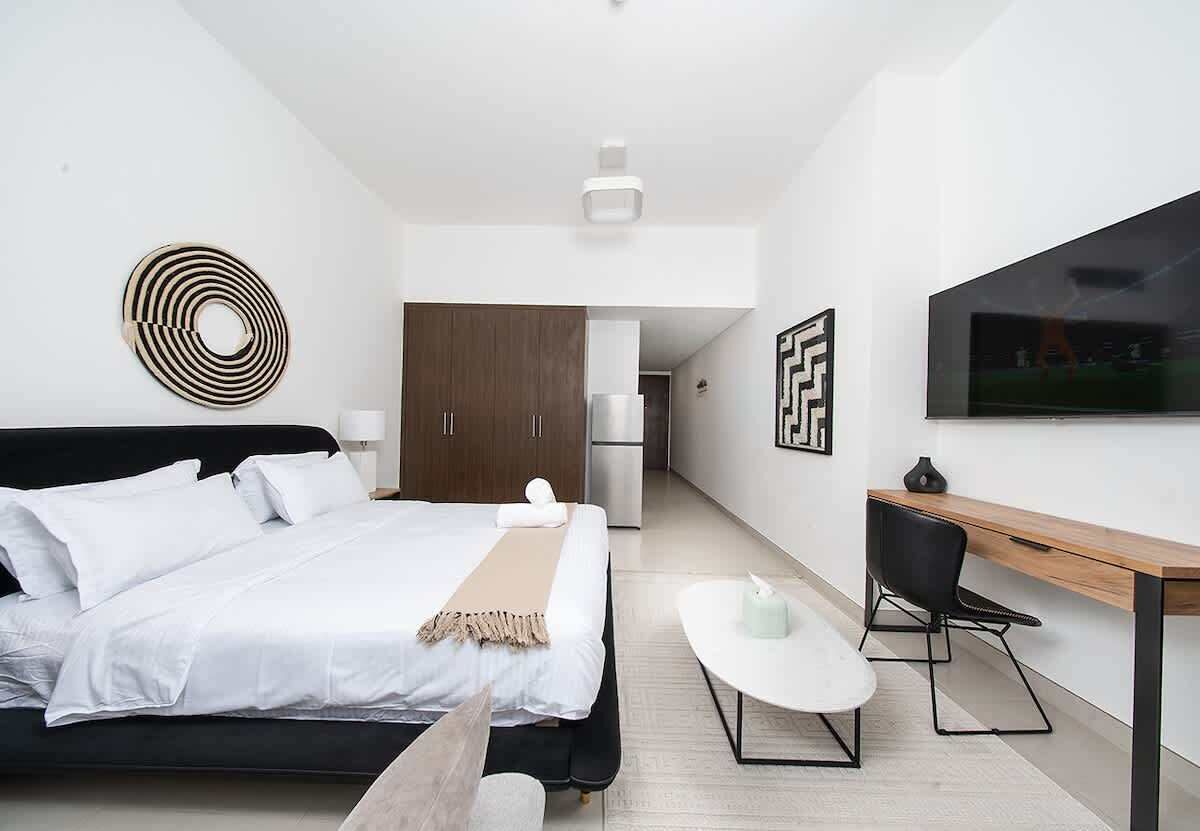 Quarto de hotel moderno com cama, escrivaninha, cadeira e televisão na parede.