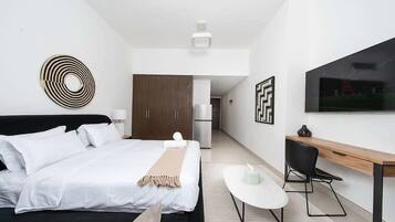 Quarto de hotel moderno com cama, escrivaninha, cadeira e televisão na parede.