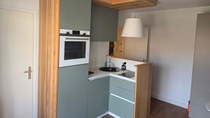 A compact kitchen with a built-in oven, a sink, and a wooden accent wall. - Modern and functional apartment near the beach and downtown (Paris)