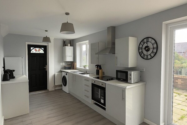 A modern kitchen with a built-in washing machine, a microwave, and a clock on the wall.