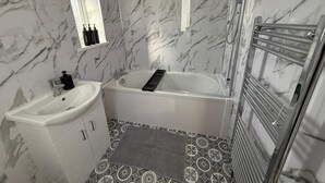 Un bagno con parete in marmo, una vasca, un lavandino e una doccia.