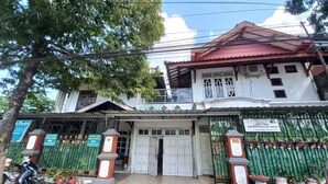 Um edifício de dois andares com entrada fechada por grades, uma placa e plantas em vasos.
