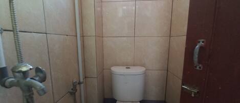 A small, tiled bathroom with a toilet, a shower, and a door with a handle.