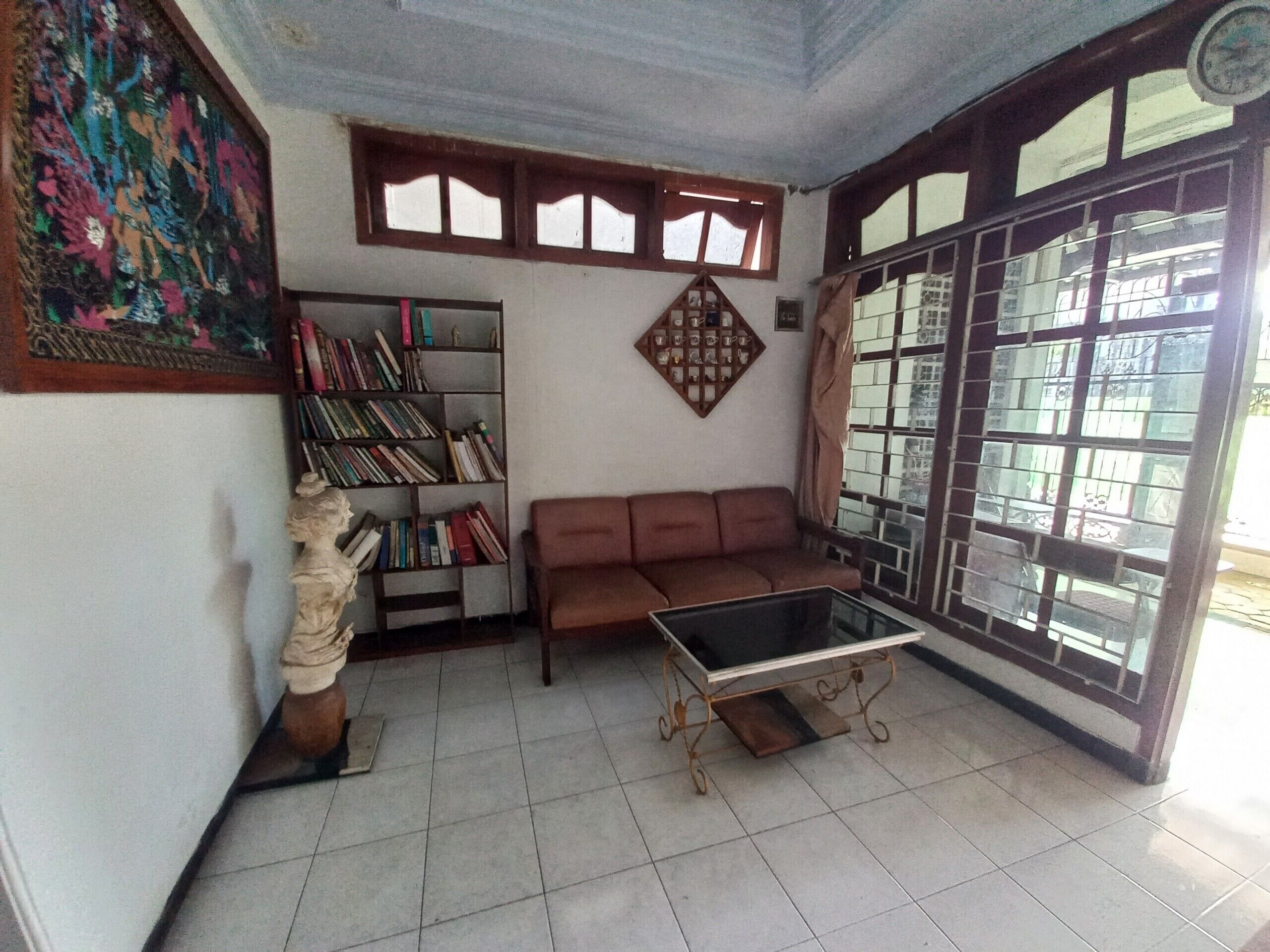 A room with a bookshelf, a brown sofa, a glass coffee table, and a decorative wall piece.
