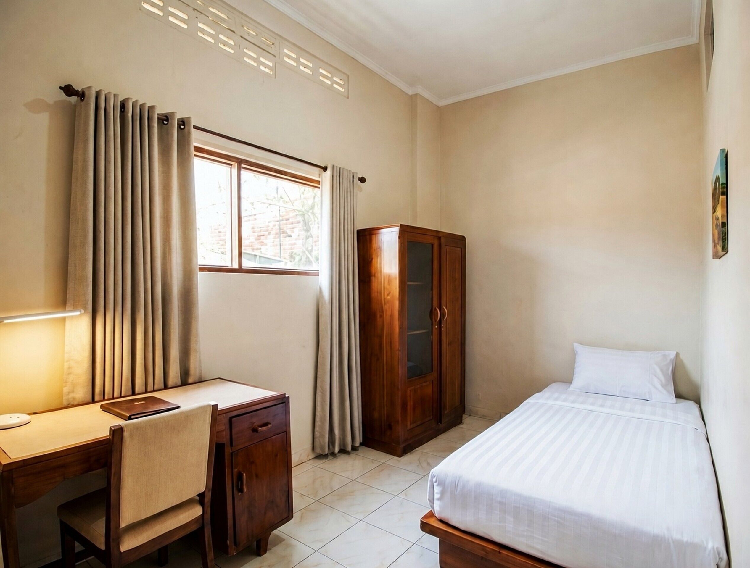 Un dormitorio con cama, escritorio con silla, armario y ventana con cortinas.