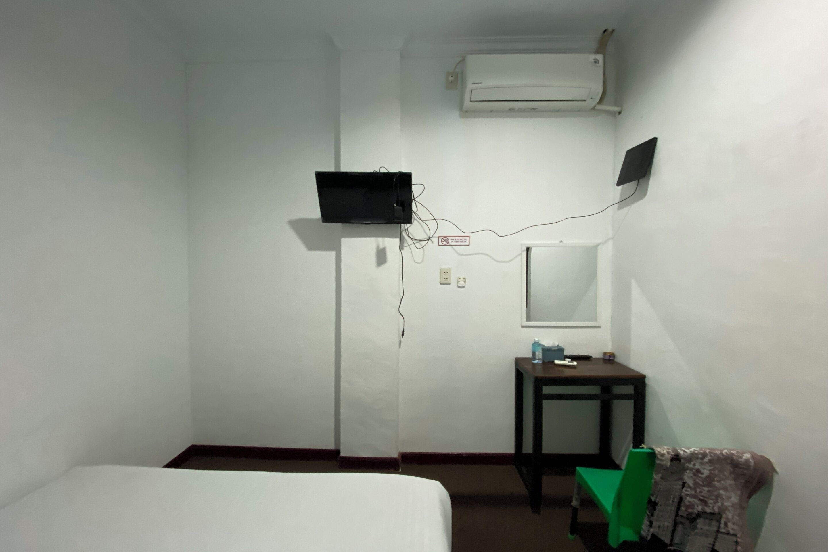 A hotel room with a bed, a desk, an air conditioner, and a television mounted on the wall.