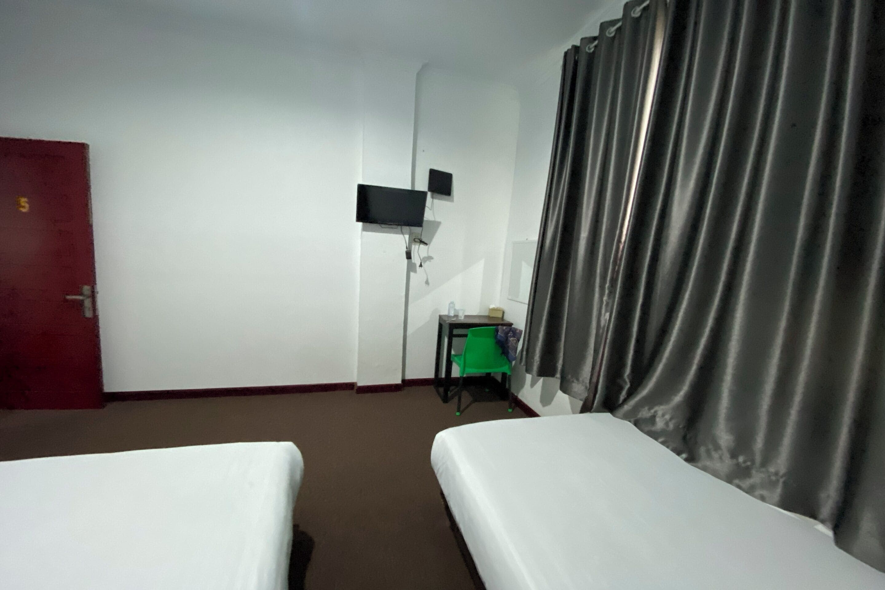 A hotel room with two beds, a desk, a television, and a door.