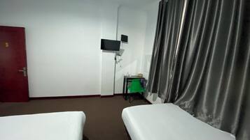 A hotel room with two beds, a desk, a television, and a door.