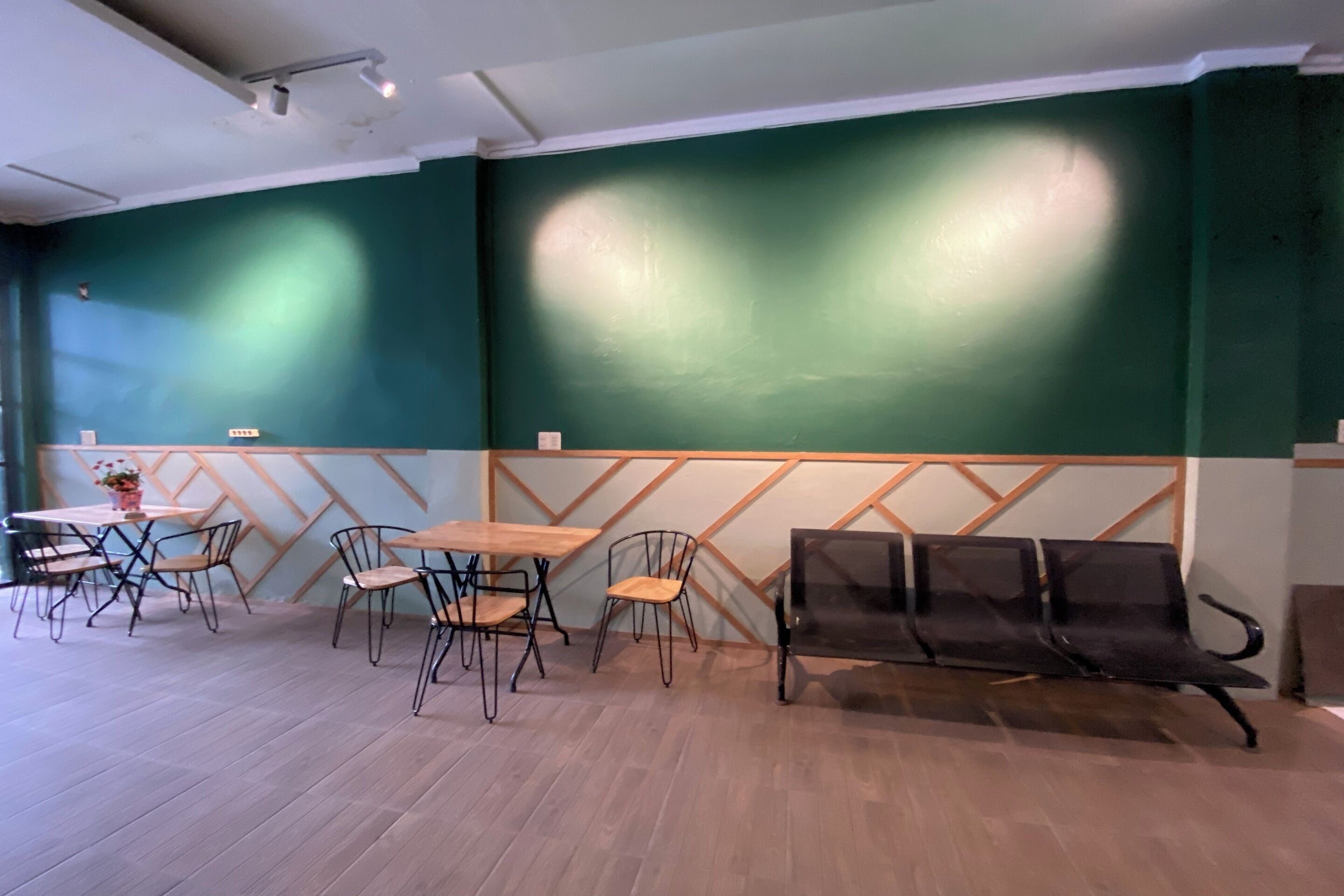 Ein Zimmer mit Holzboden, grüner Wand und einer Holzvertäfelung. Es gibt Tische, Stühle und eine Bank.