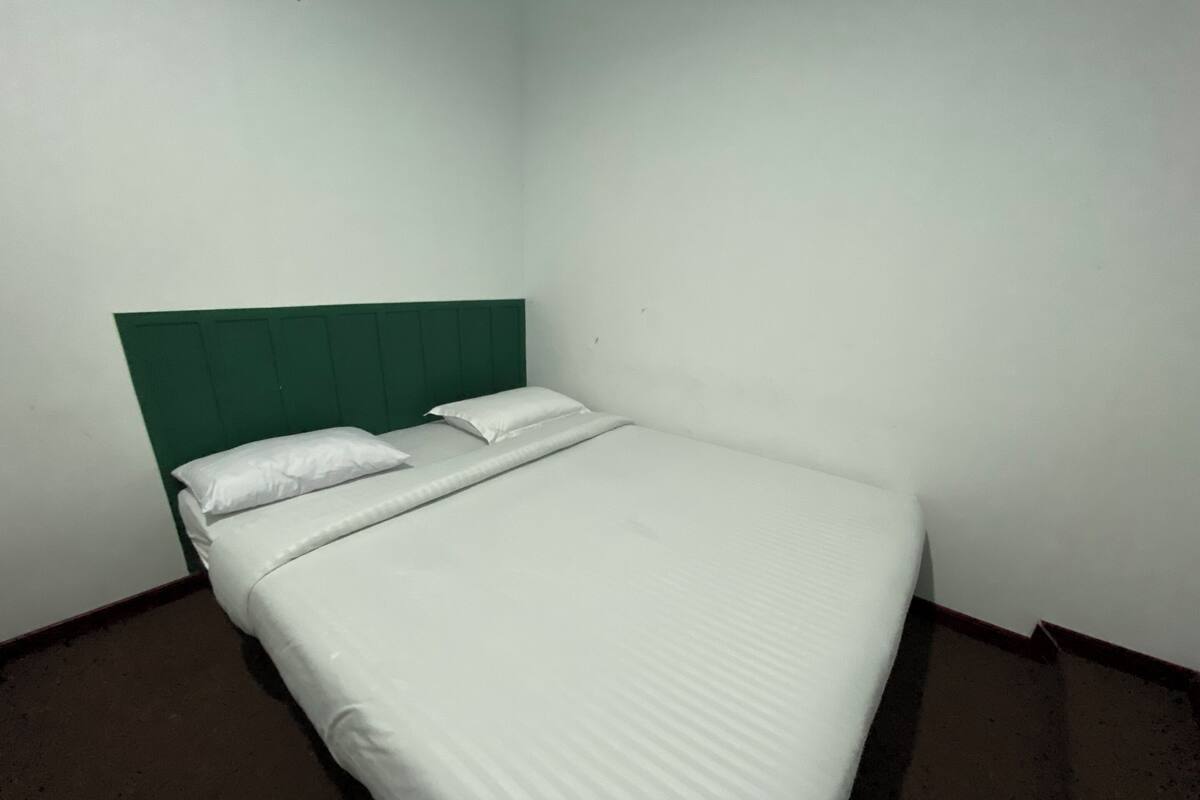 Una cama individual con ropa blanca y un cabecero verde en una habitación de esquina.