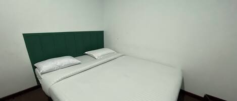 Un lit simple avec une literie blanche et une tête de lit verte, dans une chambre d’angle.