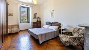A bedroom with a bed, a chair, a nightstand, a dresser, and a window with a view of mountains. - Charming Bellagio Manzoni in the heart of Bellagio with beautiful lake view (Bellagio)