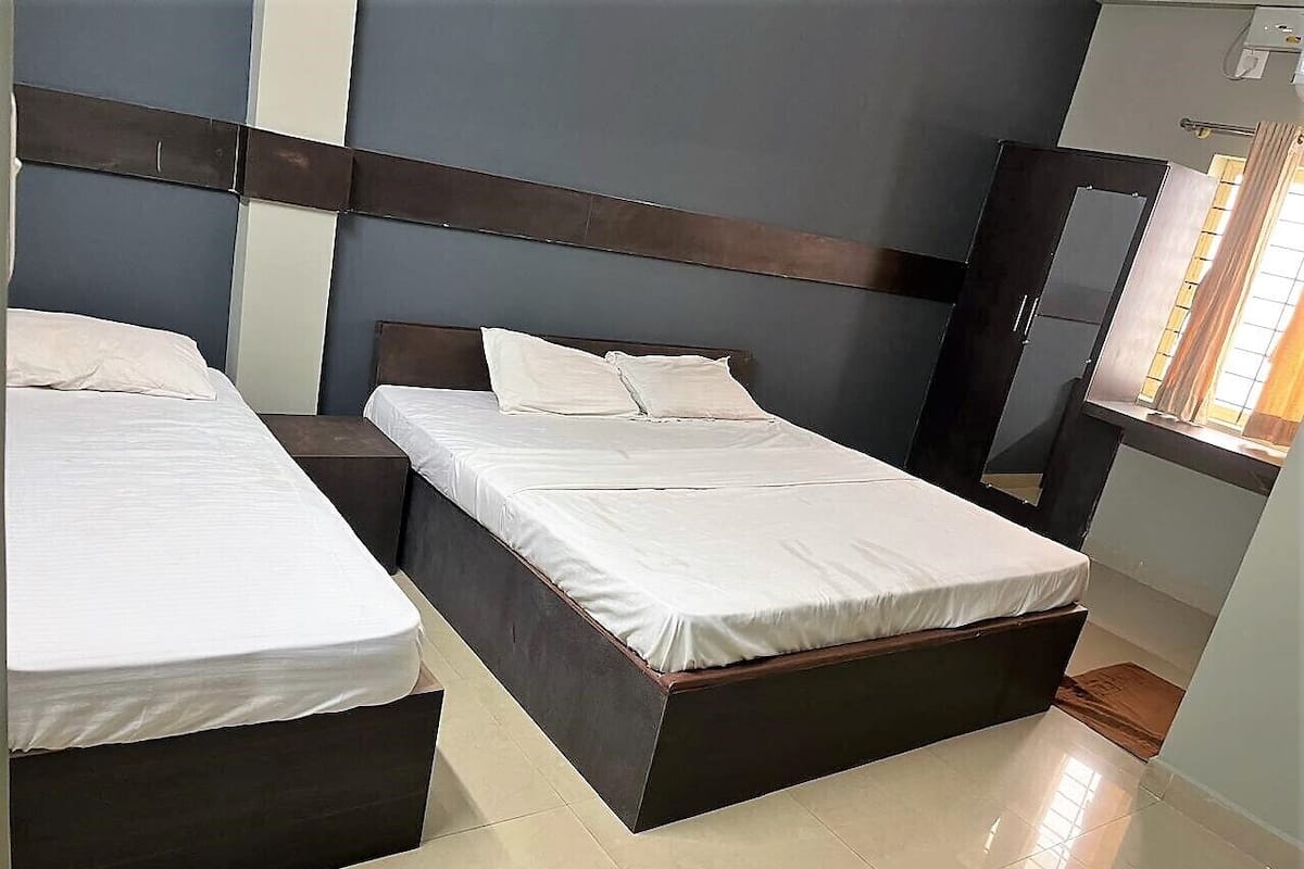 Habitación de hotel con dos camas, cabecero oscuro, ventana con cortinas y suelo de baldosas.