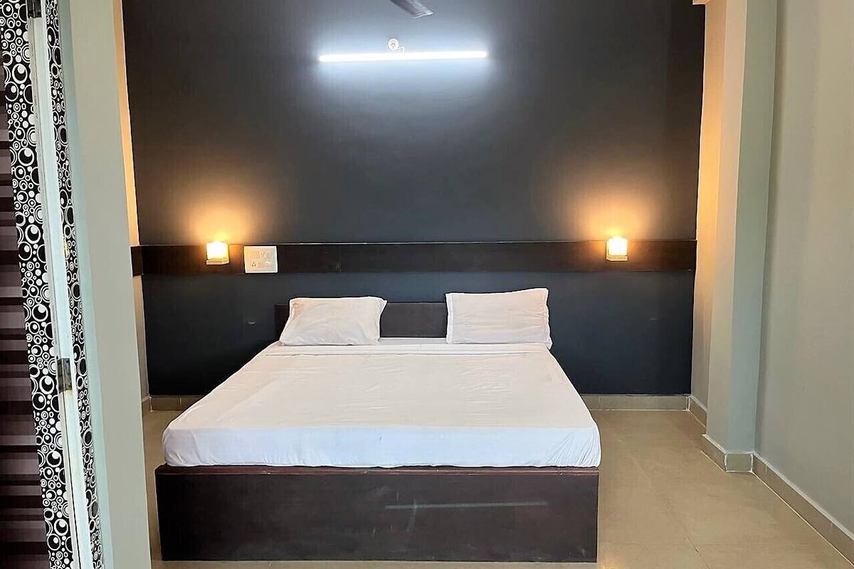 Una cama bien hecha con dos almohadas, cabecera oscura y dos lámparas de pared.