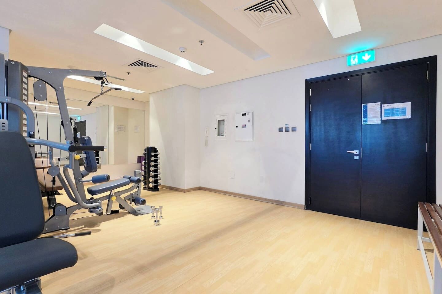 Een sportschool met trainingsapparatuur, een houten vloer, een zwarte deur en een plafond met inbouwverlichting.