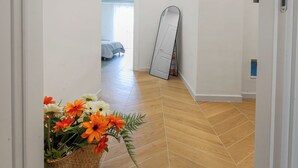 Een gang met een houten visgraatvloer, een witte deur en een spiegel die tegen de muur staat.