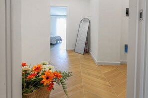 Ein Korridor mit Holzdielen im Fischgrätmuster, einer weißen Tür und einem an der Wand lehnten Spiegel.