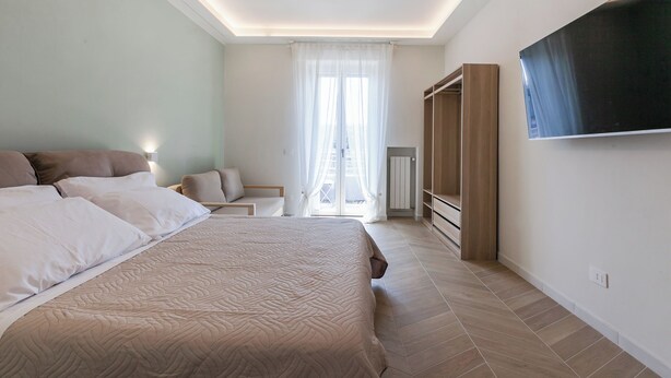Een slaapkamer met een groot bed, nachtkastjes, een kledingkast en een aan de muur bevestigde televisie.