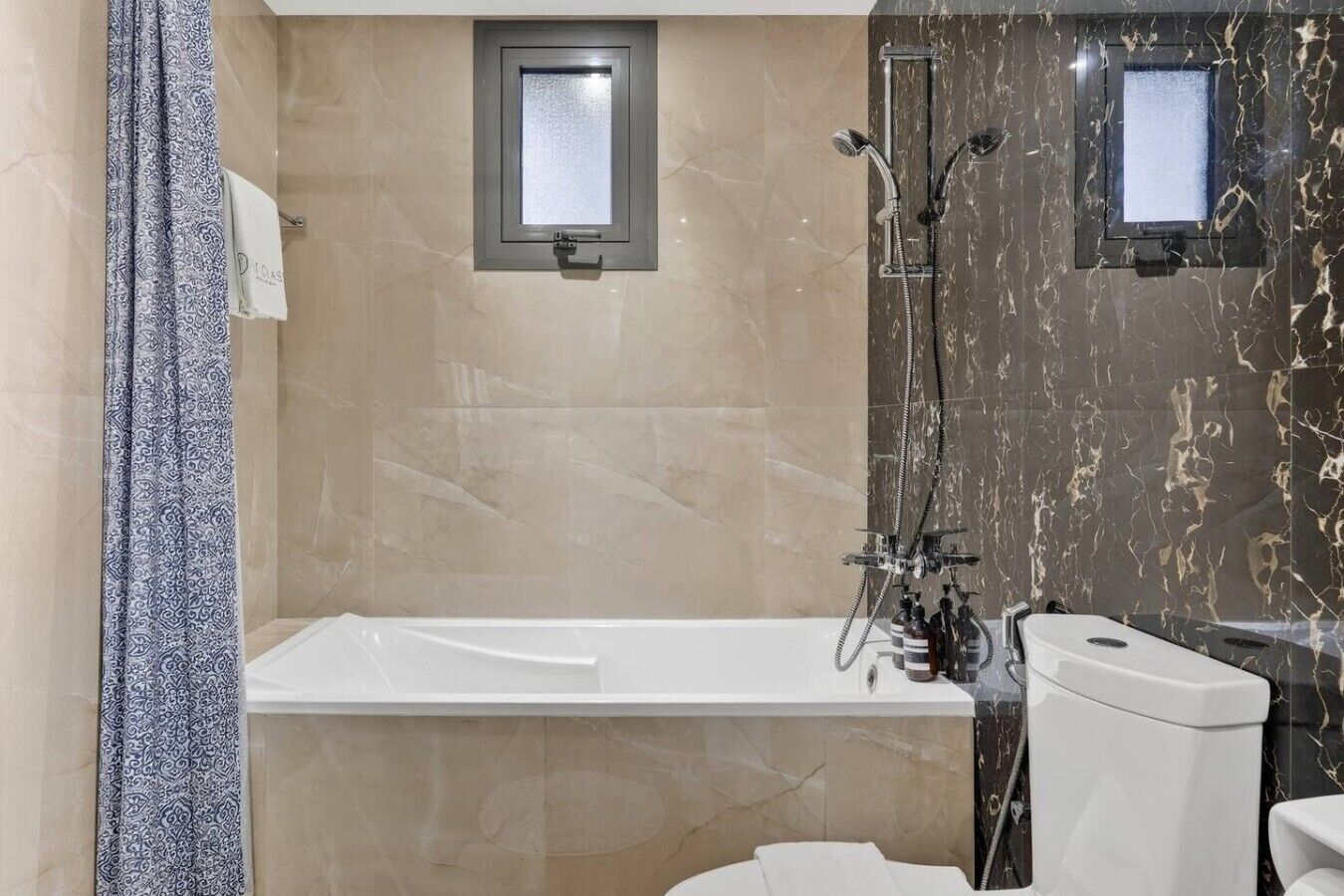 A modern bathroom with a bathtub, two showerheads, a toilet, and a towel rack.