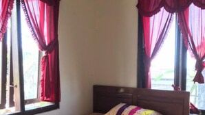 A single bed with a colorful quilt, wooden headboard, and red curtains.