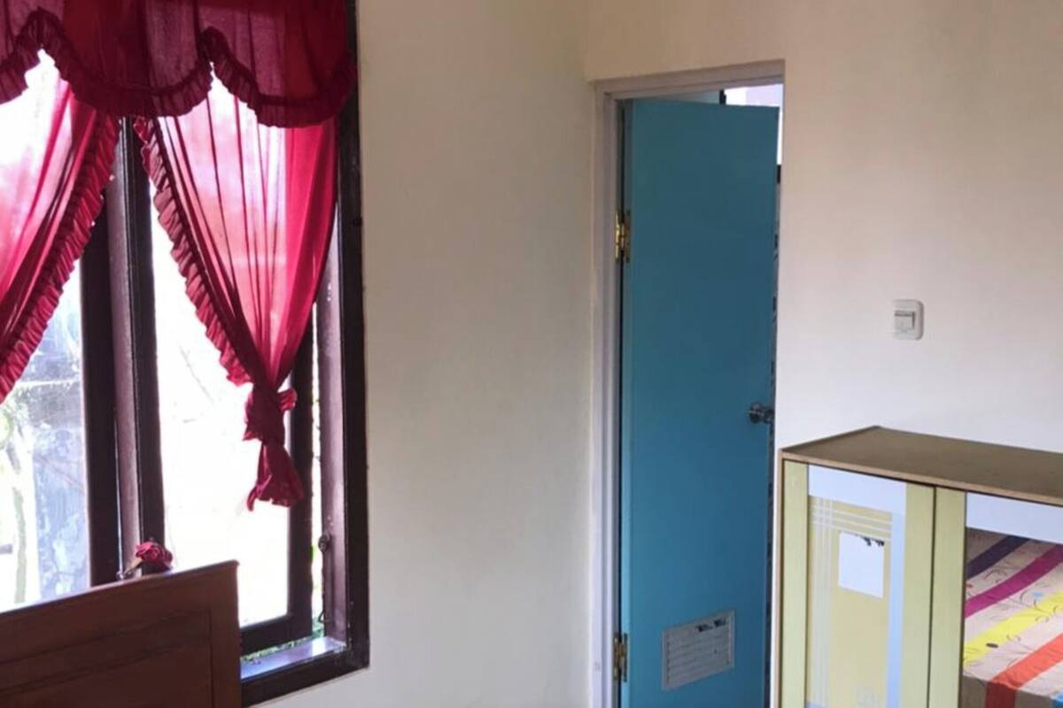 Un dormitorio con cama, armario, ventana con cortinas y puerta que da a otra habitación.