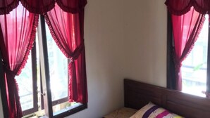 A single bed with a colorful bedspread, a wooden headboard, and red curtains on a window.