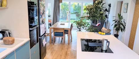 A modern kitchen with a dining area, wooden flooring, and large windows.