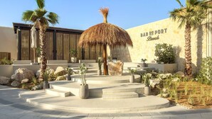 A hotel entrance with a palm tree, a thatched structure, and a sign reading 'BAR DU PORT Beach'.