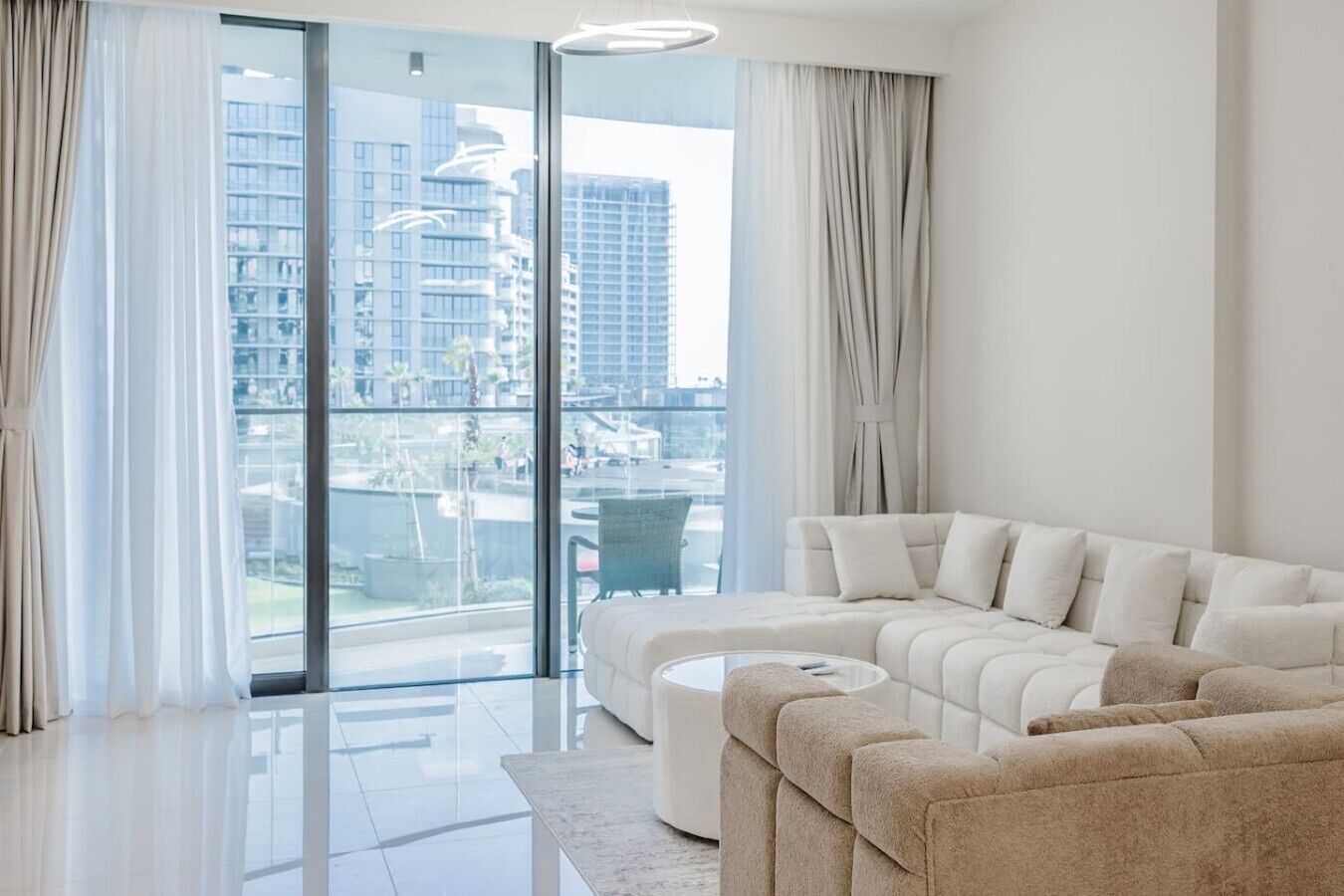 A modern living room with a large sectional sofa, a glass coffee table, and a view of a cityscape through floor-to-ceiling windows.