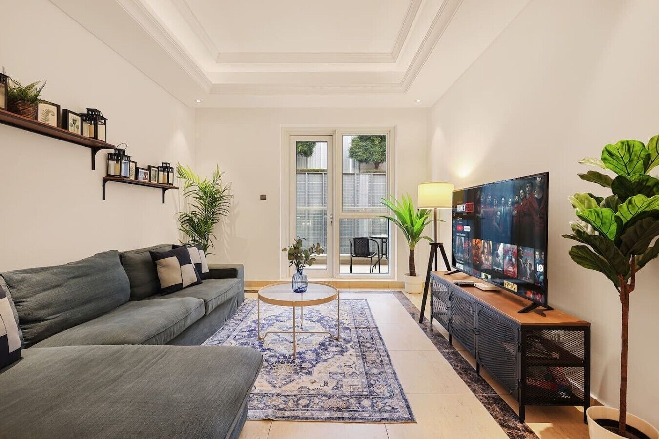 Un salon avec un canapé gris, une table basse, un téléviseur et une grande fenêtre.